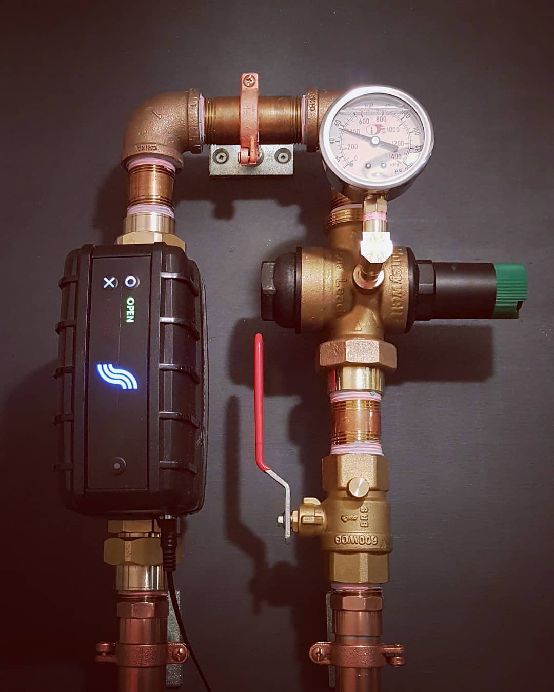 Brass plumbing with pressure gauge with water shut-off valve on a dark background